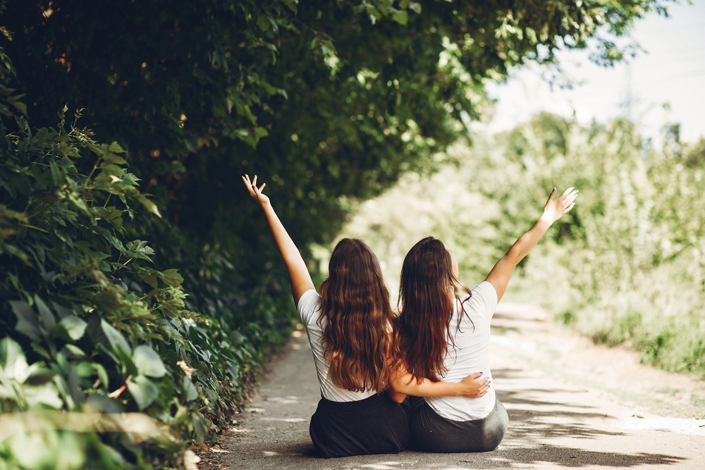 Zwei Frauen sitzen in der Natur und werfen die Hände in die Luft